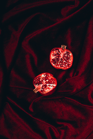 top view of ripe garnet halves on red velvet fabric background