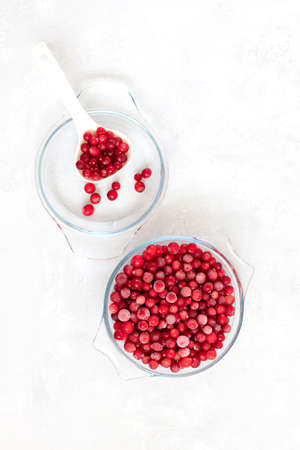 Frozen red berries on a white background. Frozen cranberries in a glass bowl. Vegan food. Vertical orientation. View from above.