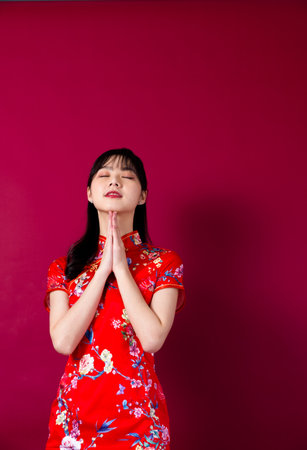 Smiling asian young woman in traditinal red cheongsam dress pointing hand to empty space on red background.