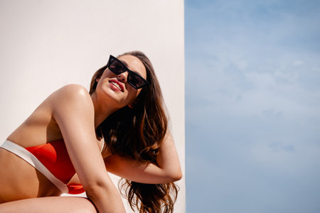 Beautiful young woman in bikini adjusting hair and smiling against white background outdoors