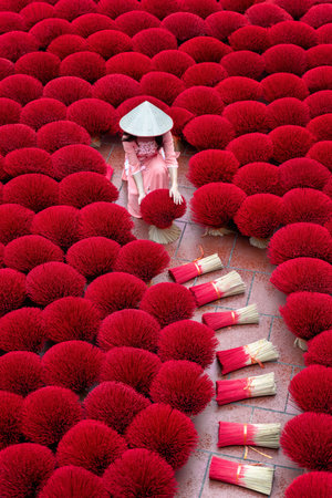 Asian woman wearing ao dai dress with Incense sticks drying outdoor in Hanoi, Vietnam.