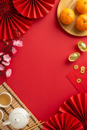 Celebrate Chinese New Year in Style: vertical top view lavish table arrangement featuring fans, green tea setup, placemat, Feng Shui items, fruits on red surface, perfect for conveying festive wishes