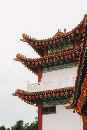 Vertical view from bottom to top of the picturesque roof of the Chinese Temple, on which red and yellow paper lanterns hang. The temple is decorated with figures of dragons. Eastern religion.