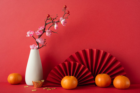 A festive arrangement celebrating Chinese New Year 2025 features tangerines, cherry blossoms, and red fans. This colorful scene evokes cultural traditions and festive joy